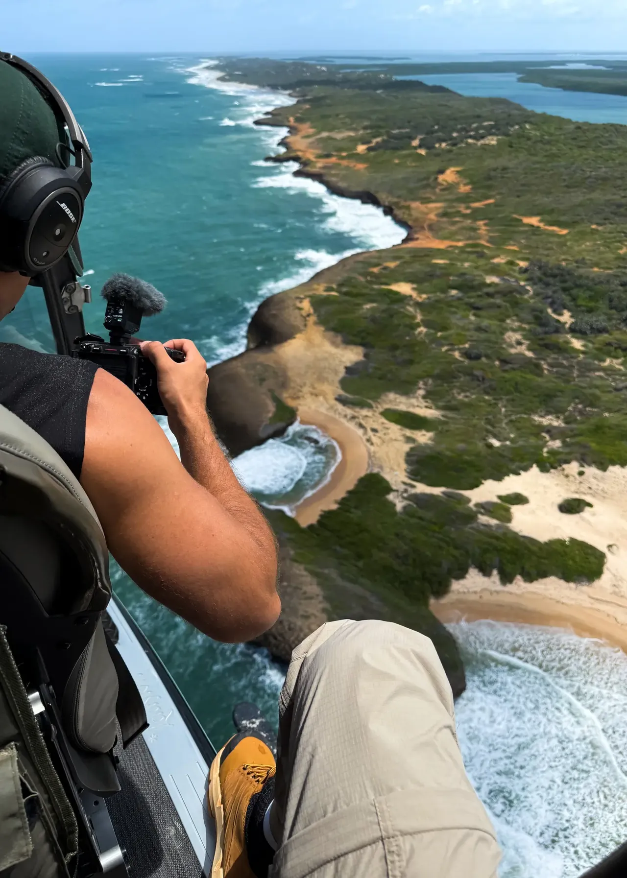 Filming from an open helicopter above a coastline