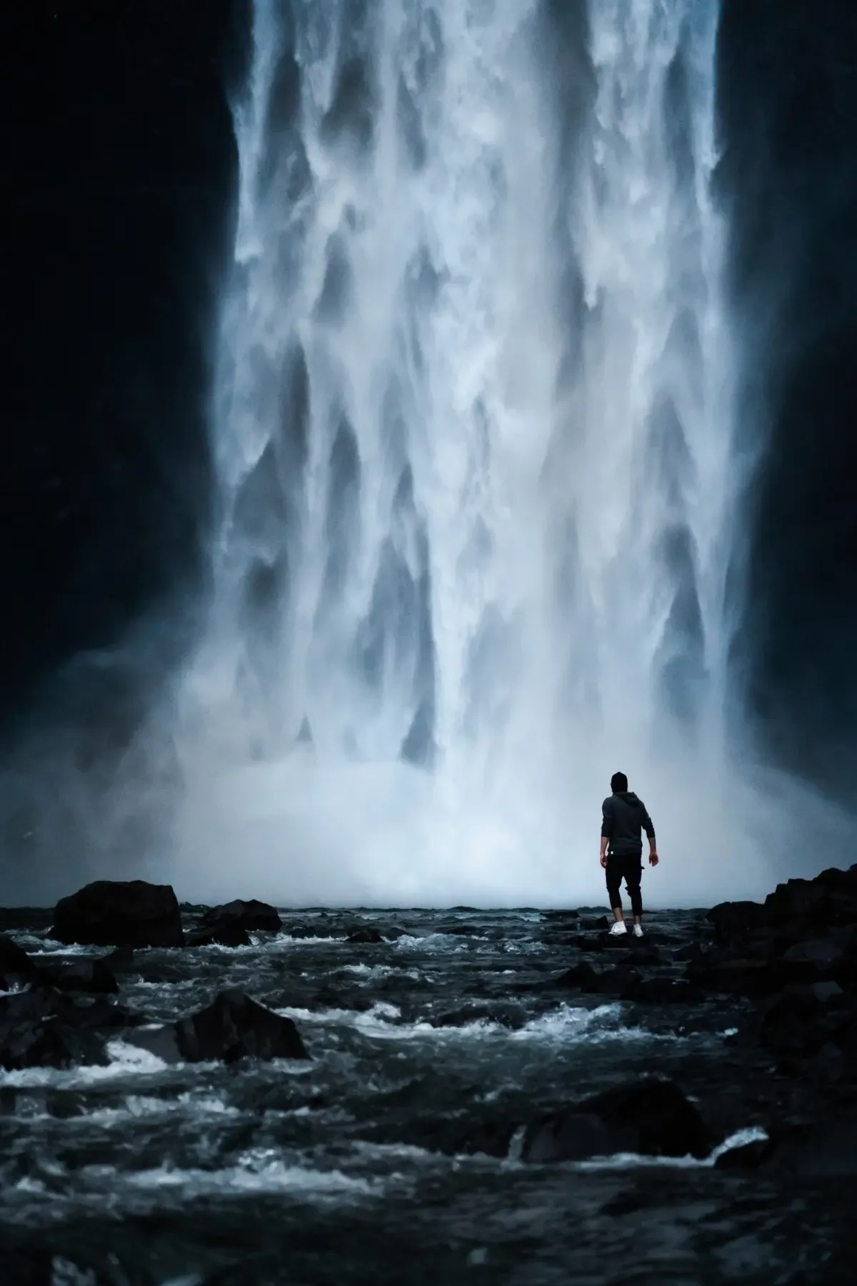 A lone figure standing before a vast waterfall