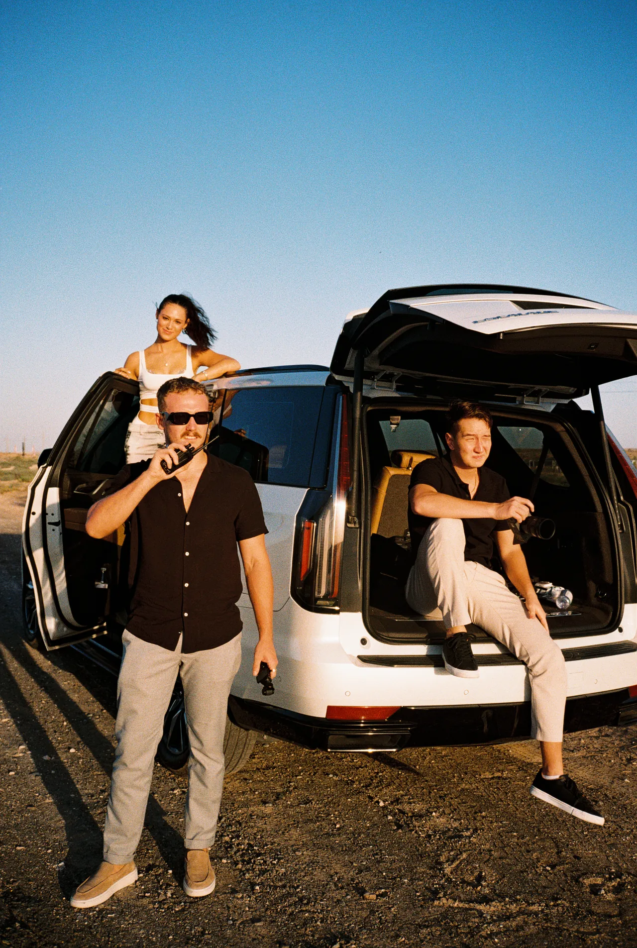 Production crew with a radio and camera beside a white SUV in the desert