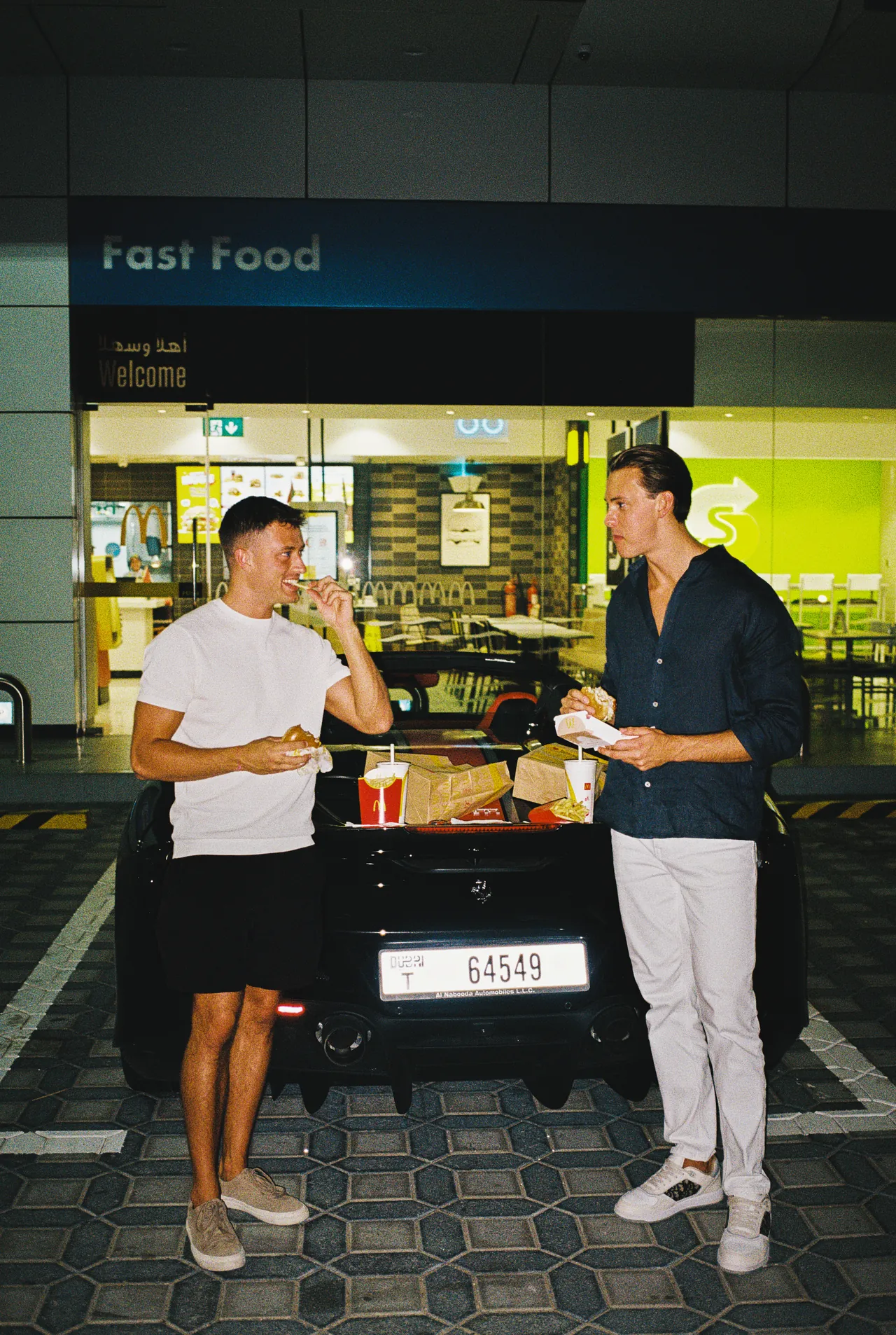 Two friends eating fast food on the back of a Ferrari late at night